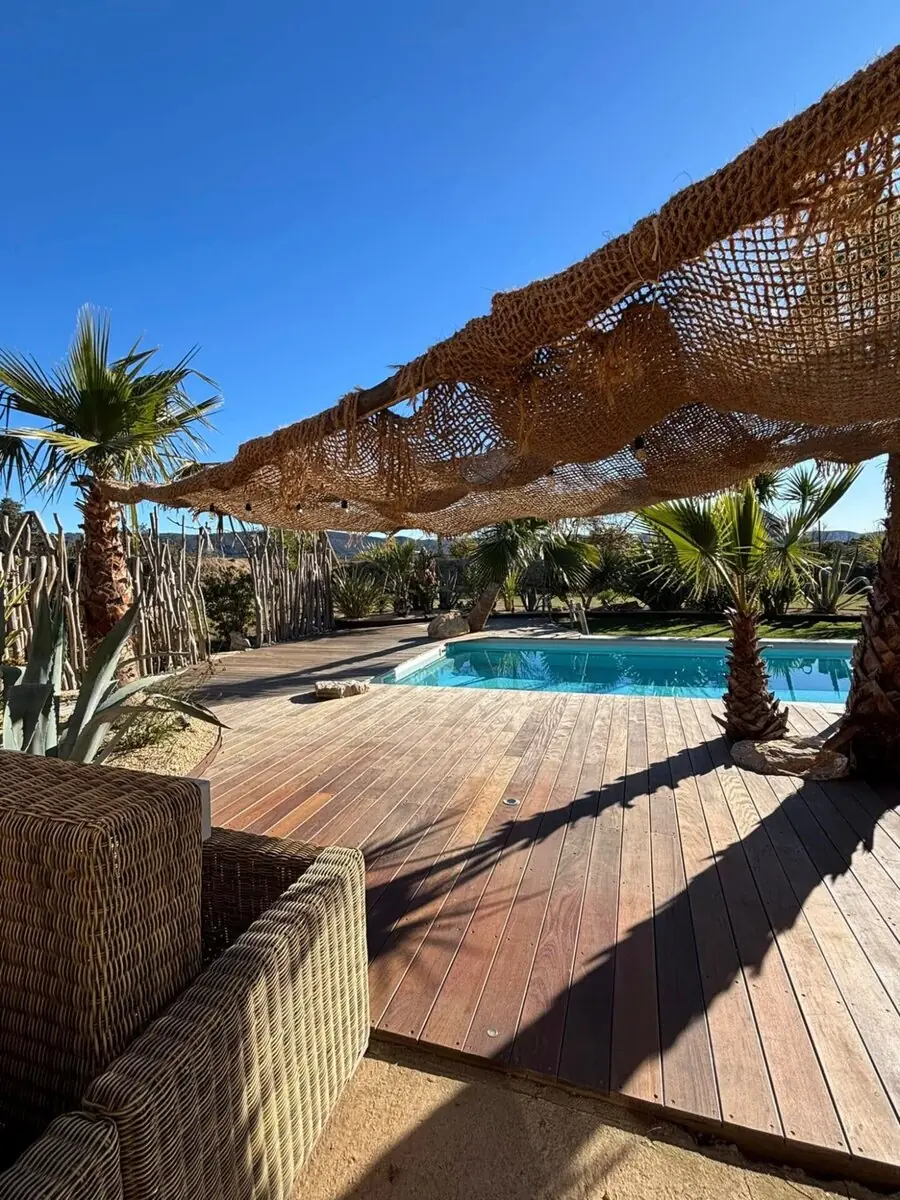 Terrasse en bois autour d'une piscine, voile d'ombrage et palmiers